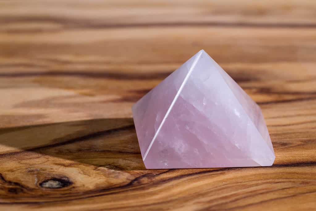 close up of a rose quartz pyramid on a wooden background, this stone is known as the stone of the heart, and promotes unconditional love.can represent heart chakra